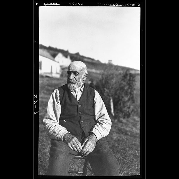 Monsieur Bichard, un homme d'âge avancé, assis dehors sur une chaise à Grand-Grève, Gaspésie, 1922, Musée canadien de l’histoire, Fonds Marius Barbeau, 57373.